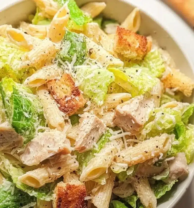 A bowl of fresh Caesar Pasta Salad with romaine, croutons, and parmesan cheese.