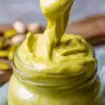 Delicious pistachio cream in a jar with a spoon, perfect for desserts.